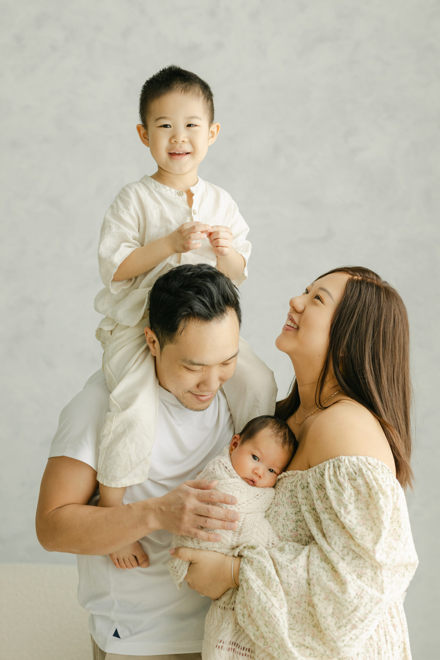 family photo of a boy on his dad's shoulders while mother is holding her newborn baby