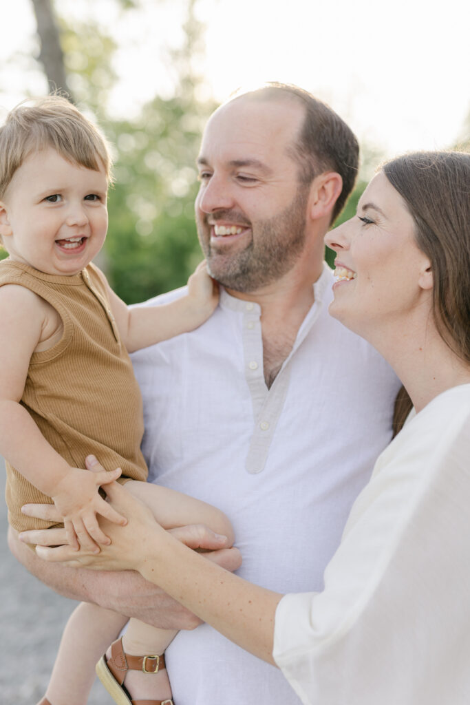 A toddler giggles while sitting in dad's arms with mom close by