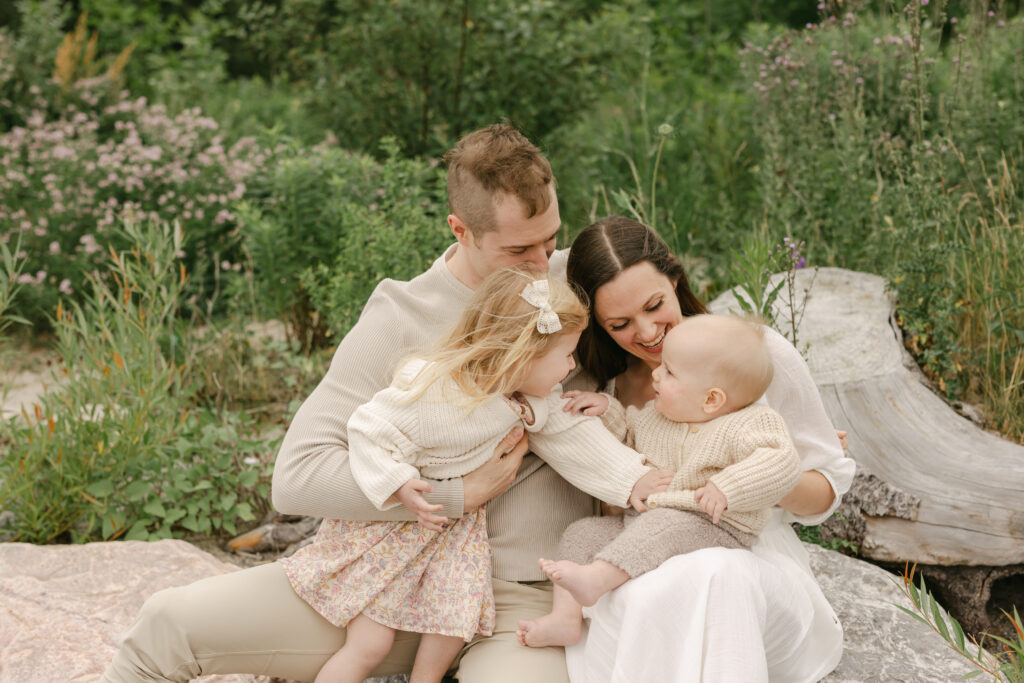 a mom and dad hug their kids while the little girl tickles her little brother