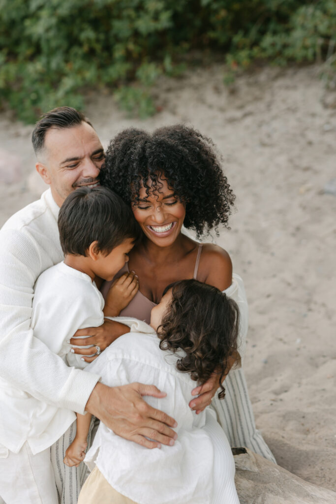 A mother and father laughing and hugging their two boys at a Toronto beach