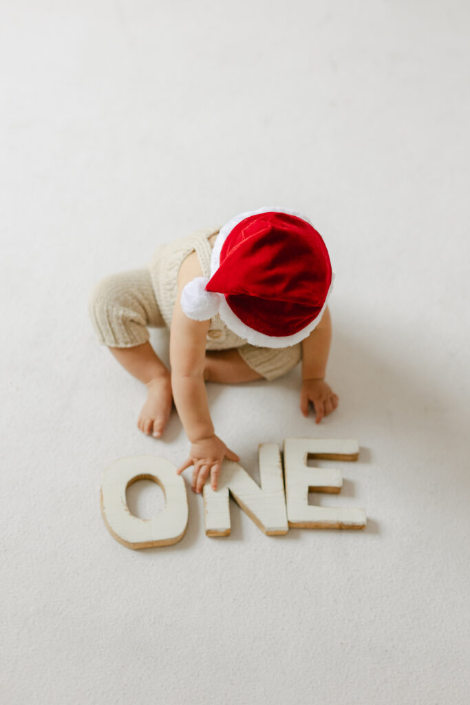 Baby wearing a Christmas hat and holding a wooden one sign