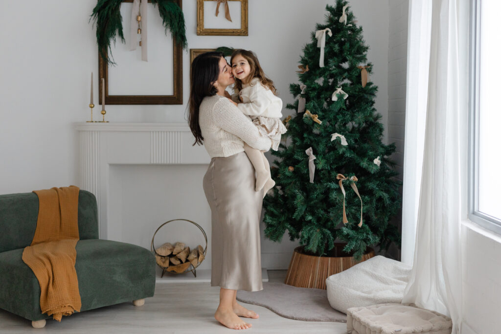 A mother is holder her daughter by the Christmas tree in a Toronto studio