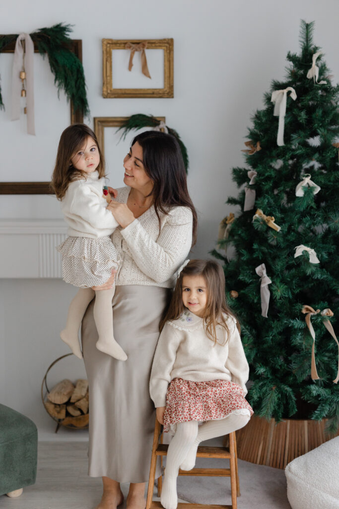 A mother and her two daughters are posing by the Christmas tree in a studio in Toronto